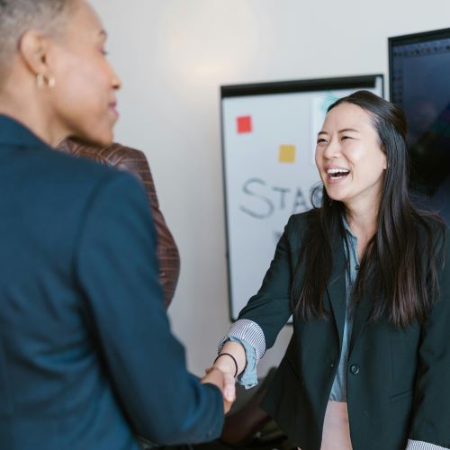 Two people smile and shake hands in a meeting room